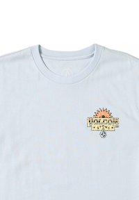 Camiseta de algodón de color azul claro con cuello redondo; presenta un colorido logo 'Volcom Stone' en el lado izquierdo del pecho. Textura suave, diseño casual.