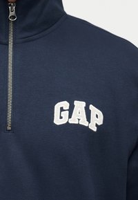 Παντελόνι quarter-zip σε ναυτικό μπλε χρώμα με λευκό κέντημα λογότυπου GAP στο αριστερό μέρος του στήθους.