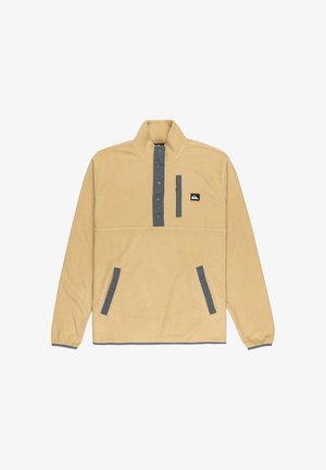 Vaalea ruskea fleece-pullovaihteinen korkealla kauluksella, harmaat yksityiskohdat, napit ja sivutaskut. Rinnassa on pieni logo.