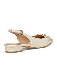 Zapato de piel beis tipo slingback con un pequeño tacón cuadrado, que presenta una punta redondeada y detalles de hardware dorado en la parte frontal. Textura suave.