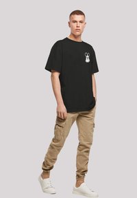 Svart t-skjorte med korte ermer og hvitt tegneser mus-design, parret med lyse khaki cargo-bukser og hvite joggesko.