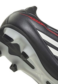 Chaussure de soccer Adidas Copa noire et blanche avec des crampons noirs sur une semelle blanche, montrant du cuir texturé et un détail de marque rouge.