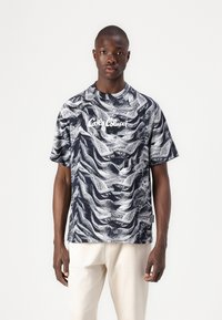 Short-sleeved, navy T-shirt with white abstract wave pattern. Features a round neckline and front logo text "Café Con Leche" in white.