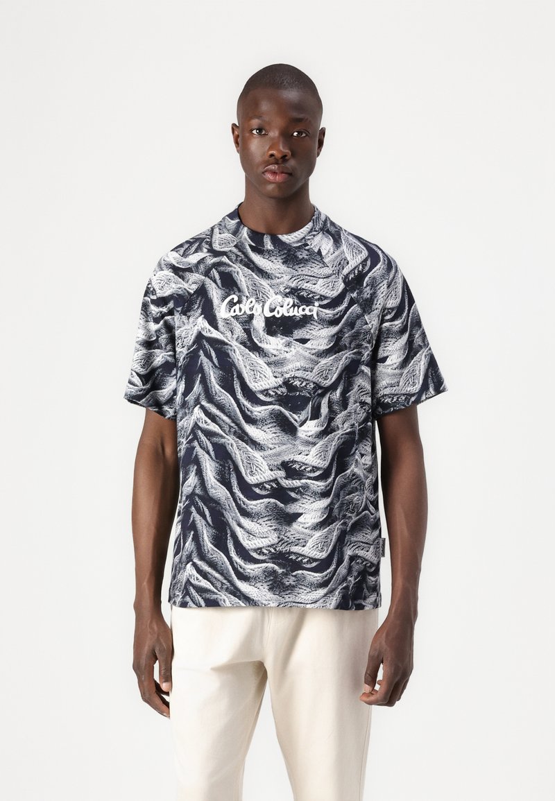 Short-sleeved, navy T-shirt with white abstract wave pattern. Features a round neckline and front logo text "Café Con Leche" in white.