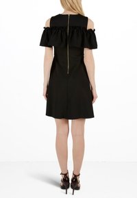 Svart klänning med avskuren axel, rynkdetaljer, figurnära liv och A-liniekjol. Bakre dragkedjestängning går ner till midjan. Kombinerad med remsandaler.