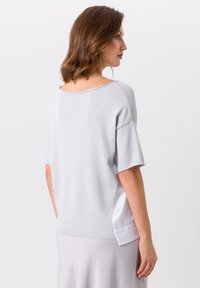 Pull en tricot gris clair à manches courtes, coupe ample, col arrondi et tissu blanc lisse contrastant sur les côtés.