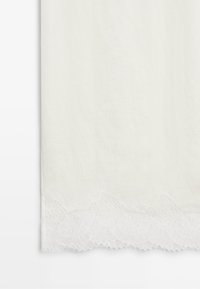 Witte stof met een delicate geschulpte kanten rand met bloemmotieven langs de onderkant.
