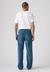 Jeans din denim de un albastru deschis, cu o croială lejeră și tăietură dreaptă. Tricou din bumbac alb vizibil, purtat cu adidași casual.