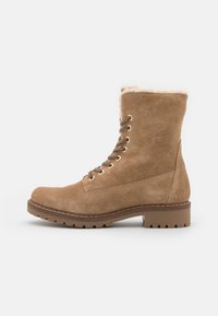 Botines de ante color marrón con forro de pelo, punta redonda y diseño de cordones. Presentan ojales metálicos y una suela rugosa y texturizada.