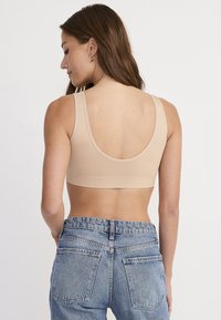 Naadloze naakte bralette met brede bandjes, een ronde rug en een gladde textuur. Gecombineerd met hoogwaist lichtblauwe denim jeans.
