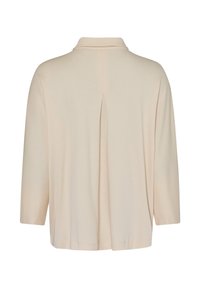 Chemise beige à manches longues avec un col et un pli central qui descend dans le dos.