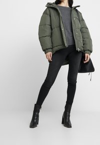 Doudoune vert olive à capuche, fermeture éclair et poignets côtelés, associée à un jean skinny noir et des bottines noires à talons.