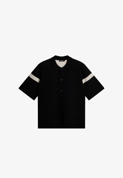 Svart kortärmad polotröja i texturerad tyg, med en vit horisontell rand på ärmarna. Framknappning, klassisk krage.