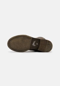 Suela de bota de ante marrón con un acabado texturizado y ligera curvatura. Presenta un tacón de madera marrón y una marca en relieve en la plantilla.