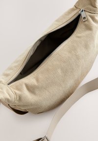 Bēšs kordurojas soma ar rāvējslēdzēja aizdari, gluda virsma un plata siksna no tā paša auduma. Iekšpuse oderēta citā krāsā.