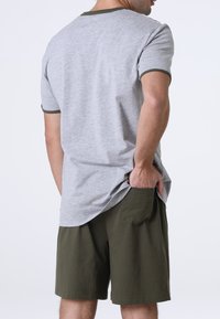 T-shirt grigia in cotone con bordi verdi; abbinata a pantaloni corti verde oliva. La T-shirt ha maniche corte e una vestibilità comoda, pantaloni corti con tasche laterali.