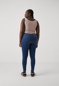 Tank top with horizontal stripes in orange, blue, and yellow, paired with blue skinny jeans. Footwear features black and tan design.