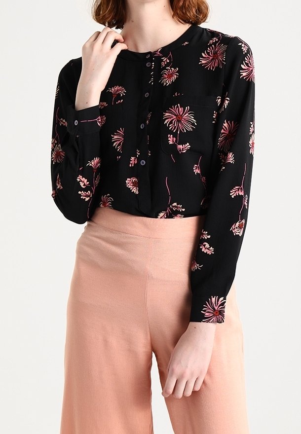 Svart knäppt blus med små rosa blommönster, med långa ärmar, rund halsringning och en liten bröstficka.