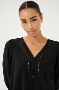 Zwarte blouse met een V-hals, knoopsluiting en decoratieve kantafwerking aan de voorkant. De stof lijkt zacht met een lichte glans.