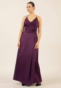Lila Satin-Maxi-Kleid mit V-Ausschnitt, gerafftem Oberteil und dünnen Trägern; verfügt über einen Seitenschlitz und eine glatte Textur. Schwarze Absätze runden das Outfit ab.