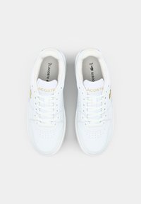 Bílé kožené tenisky s děrovanou špičkou, plochými tkaničkami a zlatými akcenty. Obsahují logo Lacoste na boku a jazyku. Texturovaná podrážka.