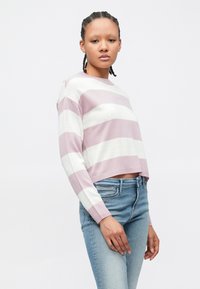 Pull court à rayures roses et blanches avec manches longues, en maille texturée. Associé à un jean slim bleu clair.