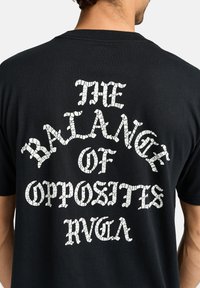 Sort T-shirt med et stort hvidt tekstgrafik på ryggen, der står "BALANCEN AF MODSATTE" i en sprukken skrifttype.