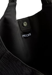 Intérieur texturé noir d'un sac à main avec un bouton-pression et une petite étiquette cousue près de l'ouverture portant l'inscription "PIECES".