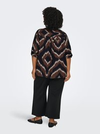 Brown and black patterned shirt with long sleeves, relaxed fit, paired with black wide-leg pants and flat shoes.