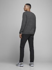 Grå langermet skjorte, mørk jeans og grå joggesko med hvite detaljer. Skjorten har rund hals og en avslappet passform.