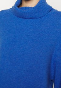 Maglione a collo alto blu realizzato in morbido tessuto a maglia, con colletto a coste e struttura liscia, dal fit rilassato e senza motivi visibili.