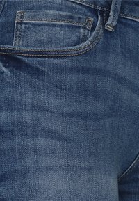 Vaqueros de mezclilla con un lavado azul oscuro, que cuentan con un bolsillo trasero y sutilezas en los detalles de la costura, mostrando una textura suave y un corte clásico.
