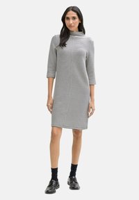 Robe rayée avec un col montant, présentant des rayures verticales noires et blanches, des manches trois-quarts et une silhouette droite.