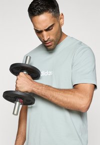 Must kaal hõbedase käepidemega, mida hoitakse parema käega. Hall lühikeste varrukatega T-särk valge brändinguga. Fookus on käsivarrel ja kaalul.