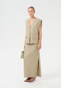 Bežs lina veste ar dziļu V veida kakla izgriezumu un priekšējo pogu aizdari, apvienota ar atbilstošu garu svārku ar sānu šķelumu un melniem augstpapēžu sandaliem.