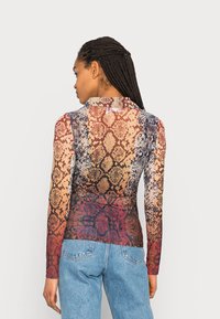 Camisa de manga longa com um padrão de pele de cobra multicolorido, design ajustado, textura transparente e decote arredondado. Usada com jeans azul claros.