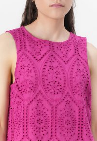 Fuchsia ermeløs topp med intrikate broderte utskjæringer med blomster- og geometriske mønstre, laget av lett stoff.