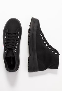 Black high-top sneakers made of textured fabric with a thick rubber sole, reinforced eyelets, and contrasting white laces.
