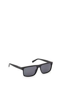 Gafas de sol negras con lentes rectangulares. Montura negra mate, detalles plateados en las varillas y lentes de un tono gris oscuro.