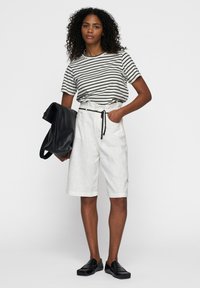 Witte linnen shorts met een trekkoord in de taille, gecombineerd met een zwart-wit gestreepte shirt met korte mouwen en zwarte instap schoenen.