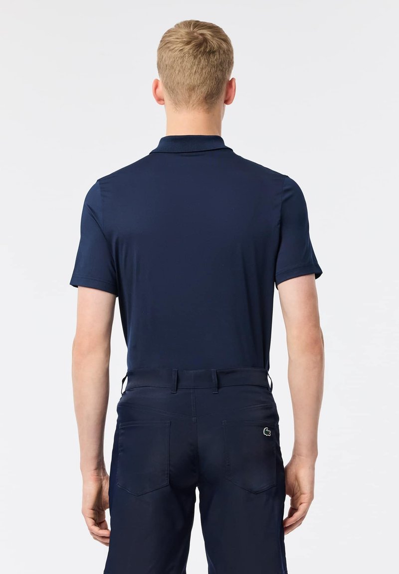 Polo shirt blu navy con una consistenza morbida, maniche corte e colletto. Indossato con pantaloni scuri abbinati, dotati di tasche posteriori e dettagli con logo.