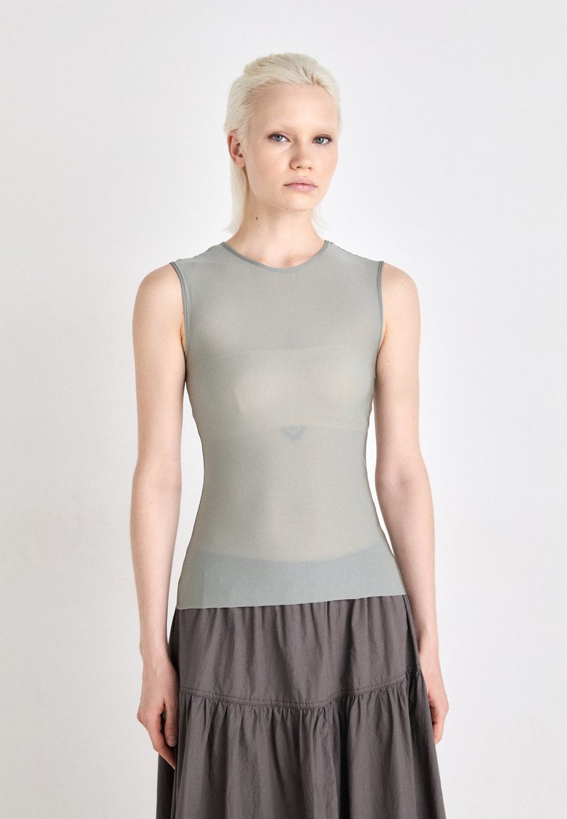 Haut sans manches gris clair en tissu lisse et extensible, conçu avec un col rond et une silhouette ajustée. Complète une jupe grise fluide.
