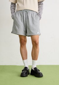 Șorturi gri din bumbac cu un tiv elastic și buzunare laterale, asortate cu șosete albe și pantofi negri cu o talpă groasă.