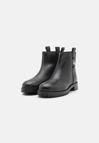 Sorte skinn ankle boots med en glat overflade, rund tå, lav blokhælt og bageste trækstropper. Har dekorative hardware på siden.