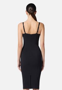 Abito nero senza maniche con spalline regolabili, silhouette aderente, zip sul retro e una fessura centrale per facilitare i movimenti. Tessuto liscio su tutta la superficie.