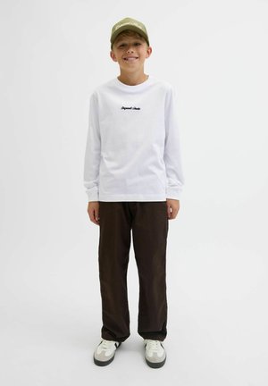 Weißes Langarmhemd mit schwarzem Text, braune Hose und grau-weiße Sneakers. Die Kappe ist olivgrün mit weißer Schrift.