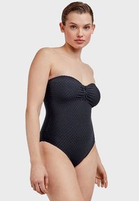 Bañador negro sin tirantes con tejido texturizado de patrón de puntos y detalles fruncidos en el centro. Diseño de pierna alta.