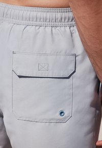 Lichtblauwe shorts met een elastische tailleband, voorzien van een klepzak aan de achterkant en een klein blauw ringetje nabij de zak.