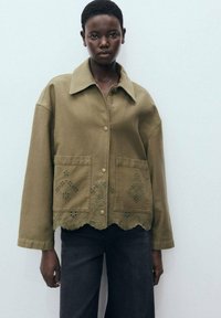 Veste en coton vert olive avec un col, fermeture à boutons, deux poches avant et broderies complexes à l'ourlet.