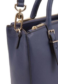 Marineblauwe leren handtas met gouden accenten, voorzien van een ritssluiting en een afneembare schouderriem. Textuur van het materiaal zichtbaar op het lichaam.